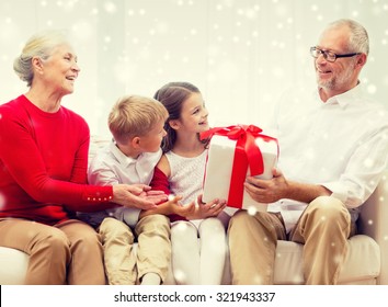 Family, Holidays, Generation, Christmas And People Concept - Smiling Grandparents And Grandchildren With Gift Box Sitting On Couch At Home