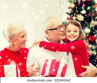 Family, Holidays, Generation, Christmas And People Concept - Smiling Grandparents And Granddaughter With Gift Boxes Sitting On Couch At Home