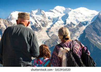 Family Holidays In Mountains. Senior Man And Woman With Their Granddaughter Admiring Snow Cover Mont Blanc Mountain In Alps. Back View. Elderly Wellness, Family Together, Healthy Lifestyle Concepts. 