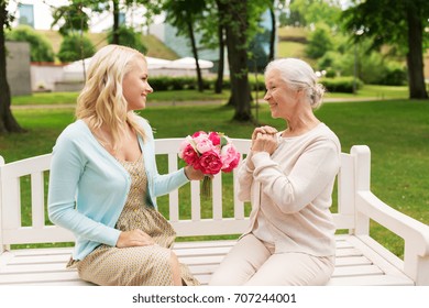 family, holidays and people concept - happy smiling young daughter giving flowers to her senior mother sitting on park bench - Shutterstock ID 707244001