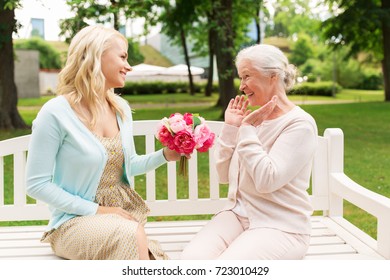 family, holidays and people concept - happy smiling young daughter giving flowers to her senior mother sitting on park bench - Shutterstock ID 723010429