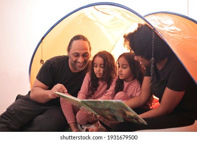 Family In A Home Camping Tent Look At A Picture Book