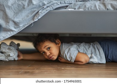 Family At Home Concept, Boy Playing Hide And Seek. Cute Afro Boy Peeking Out From Under The Bed.