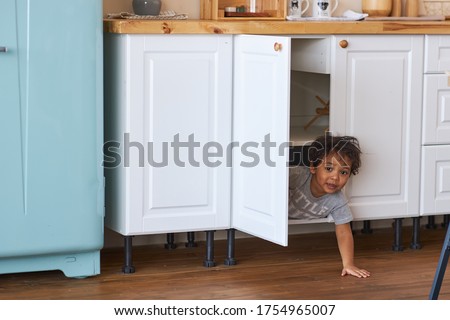 Family at home concept, little boy playing hide and seek. A happy child looks out of the closet in the kitchen.