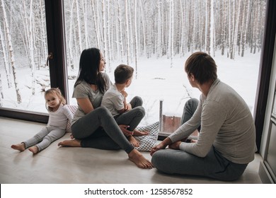 Family at home in pajamas. Daughter and son. Wake up in the morning. Hugging and kissing, looking out the window. Beautiful winter outside the window. Large windows to floor. Nice view from window.