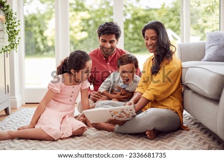 Family At Home Sitting On Floor In Lounge Reading Book Together