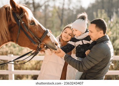 Family with horse having fun. Happy father, mother and son caress horse outdoors on a farm ranch. Dad, mom and child. Animal love. Parent and kid cuddling animal pet at sunset. Soft focus on face. - Powered by Shutterstock