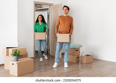 Family Housing Concept. Happy couple walking in new apartment and looking around, smiling young guy and lady holding cardboard boxes standing in modern home. Real estate dwelling, mortgage