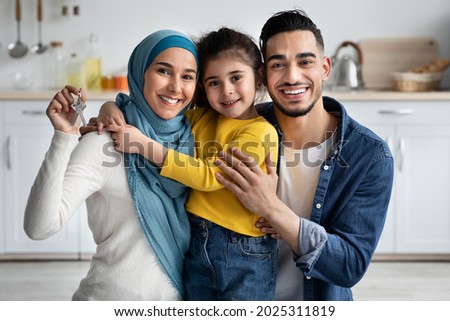 Family Housing Concept. Happy Islamic Spouses With Little Daughter Holding Home Keys In Hands And Smiling At Camera, Cheerful Arab Parents And Their Female Child Celebrating Moving, Closeup Shot