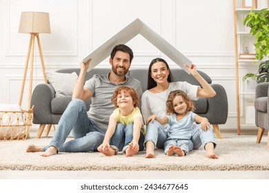 Family housing concept. Happy woman and her husband holding plastic roof while sitting with kids on floor at home