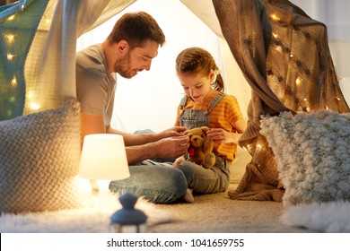 Family, Hygge And People Concept - Happy Father With Teddy Bear Toy And Little Daughter Playing In Kids Tent At Night At Home