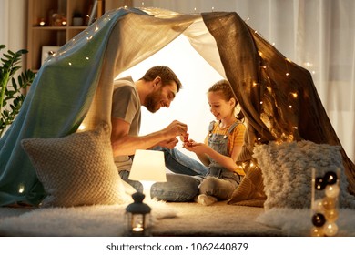 family, hygge and people concept - happy father and little daughter playing tea party in kids tent at night at home - Powered by Shutterstock