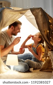 Family, Hygge And People Concept - Happy Father And Little Daughter Playing Tea Party In Kids Tent At Night At Home