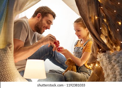 Family, Hygge And People Concept - Happy Father And Little Daughter Playing Tea Party In Kids Tent At Night At Home