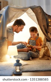 Family, Hygge And People Concept - Happy Father With Teddy Bear Toy And Little Daughter Playing In Kids Tent At Night At Home