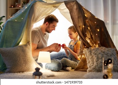 Family, Hygge And People Concept - Happy Father And Little Daughter Playing Tea Party In Kids Tent At Night At Home