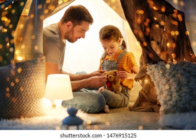 family, hygge and people concept - happy father with teddy bear toy and little daughter playing in kids tent at night at home - Powered by Shutterstock