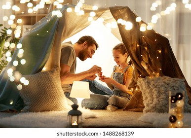 Family, Hygge And People Concept - Happy Father And Little Daughter Playing Tea Party In Kids Tent At Night At Home