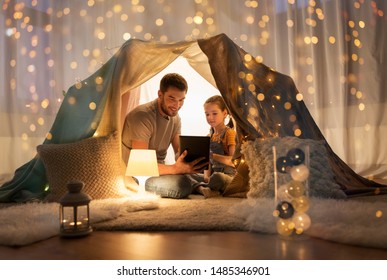 Family, Hygge And Technology Concept - Happy Father And Little Daughter With Tablet Pc Computer In Kids Tent At Night At Home