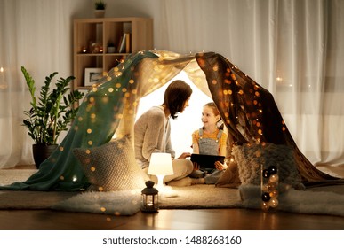 Family, Hygge And Technology Concept - Happy Mother And Little Daughter With Tablet Pc Computer In Kids Tent At Night At Home