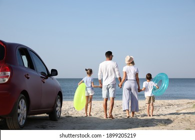 Family With Inflatable Rings Near Car At Beach