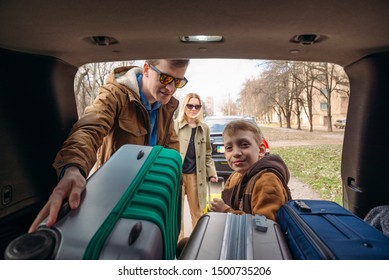 Family With Kid Putting Bag In Car Trunk. Road Trip Gathering