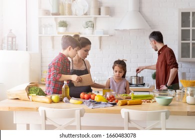 Family with kid spending time on home kitchen in morning. Parent children cooking. Mother and boy son talking to upset daughter. Father mixing boiling dish in pot on stove. Fresh vegetable on table