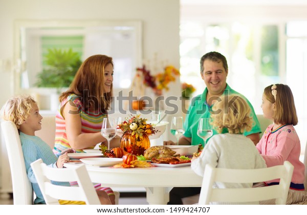 感謝祭の晩餐を食べる子供のいる家族 食卓の上の七面鳥とカボチャの焼きと秋の飾り お祝いの食事をする両親と子ども 肉を切る父と母 の写真素材 今すぐ編集