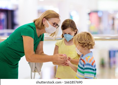 Family With Kids In Face Mask In Shopping Mall Or Airport. Mother And Child Wear Facemask During Coronavirus And Flu Outbreak. Virus And Illness Protection, Hand Sanitizer In Public Crowded Place.