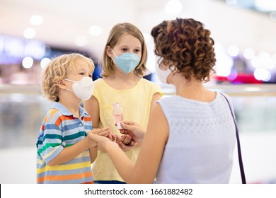 Family With Kids In Face Mask In Shopping Mall Or Airport. Mother And Child Wear Facemask During Coronavirus And Flu Outbreak. Virus And Illness Protection, Hand Sanitizer In Public Crowded Place.