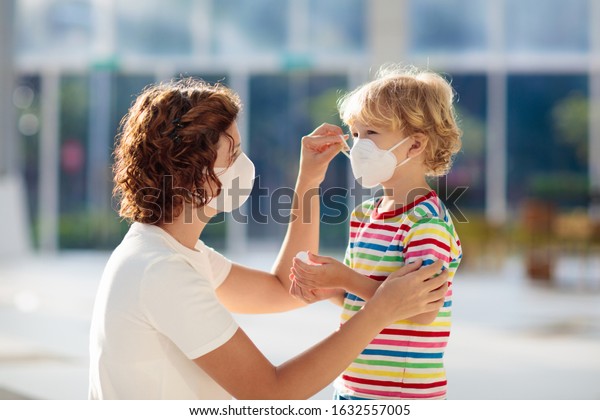 Family with kids in face mask in shopping mall or\
airport. Mother and child wear facemask during coronavirus and flu\
outbreak. Virus and illness protection, hand sanitizer in public\
crowded place.