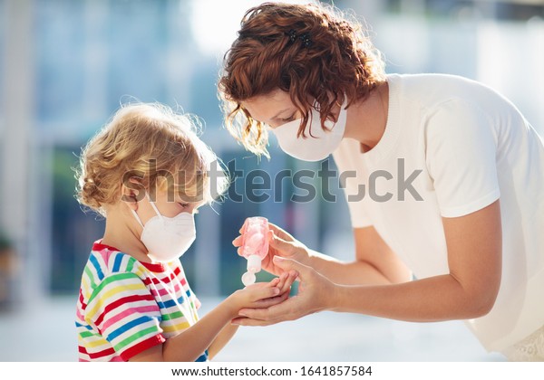 Family with kids in face mask in shopping mall or\
airport. Mother and child wear facemask during coronavirus and flu\
outbreak. Virus and illness protection, hand sanitizer in public\
crowded place.