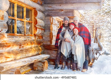 Family With Kids Outdoors On Beautiful Winter Day In Front Of Log Cabin Vacation House