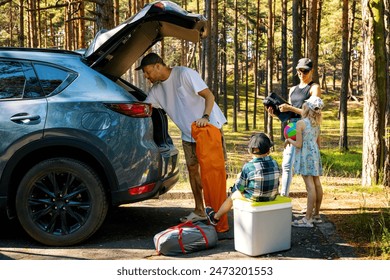 family with kids remove the camping supplies from car trunk at forest. summer vacation, road trip - Powered by Shutterstock