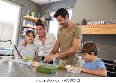 Family In Kitchen Following Recipe On Digital Tablet Together