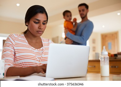 Family In Kitchen With Mother Using Laptop At Table
