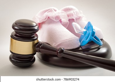 Family Law And Child Custody Concept With A Blue Pacifier And A Pair Of Pink Baby Shoes Next To A Judge's Gavel