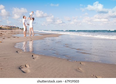 Family Leaves Footprints In The Sand As Parents Play With Baby On The Beach