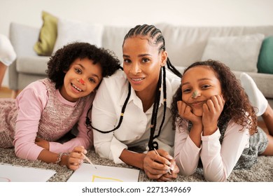 Family Leisure  Cheerful African American Mom And Two Daughters Drawing Spending Time Together Lying On Floor Smiling To Camera At Home  Happy Weekend With Mommy  Parenting Concept