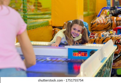 Family Leisure. Cheerful Girl Playing Air Hockey Game With Her Mum At Kids Amusement Center