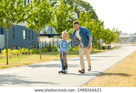family, leisure and fatherhood concept - happy father spending time with little son riding scooter in city