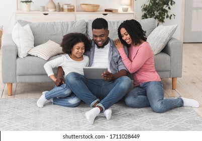 Family Leisure. Happy African American Parents And Their Little Daughter Using Digital Tablet At Home Together, Watching Videos Or Browsing Internet