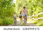 family, leisure and people concept - happy mother, father and little daughter riding bicycles in summer park