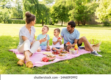 Family, Leisure And People Concept - Happy Mother, Father And Two Little Sons Having Picnic And Eating Watermelon At Summer Park