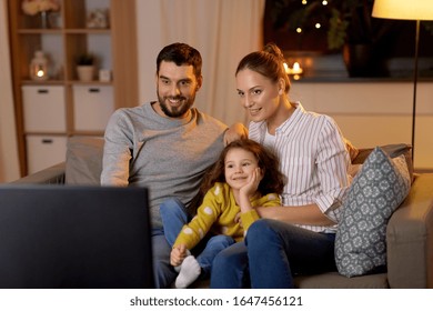 Family, Leisure And People Concept - Happy Smiling Father, Mother And Little Daughter Watching Tv At Home At Night