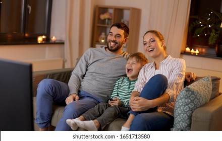 Family, Leisure And People Concept - Happy Smiling Father, Mother And Little Son With Remote Control Watching Something Funny On Tv At Home At Night