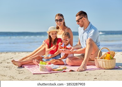 family, leisure and people concept - happy mother, father and two daughters having picnic on summer beach and eating strawberries