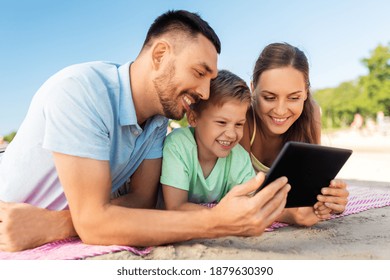 Family, Leisure And People Concept - Happy Smiling Mother, Father And Son With Tablet Computer Laying On Summer Beach