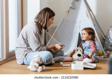 Family, Leisure And People Concept - Happy Mother And Little Baby Daughter Playing Doctor At Home