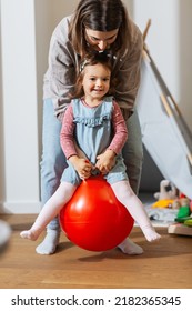 family, leisure and people concept - happy mother playing with little baby daughter bouncing on hopper ball at home